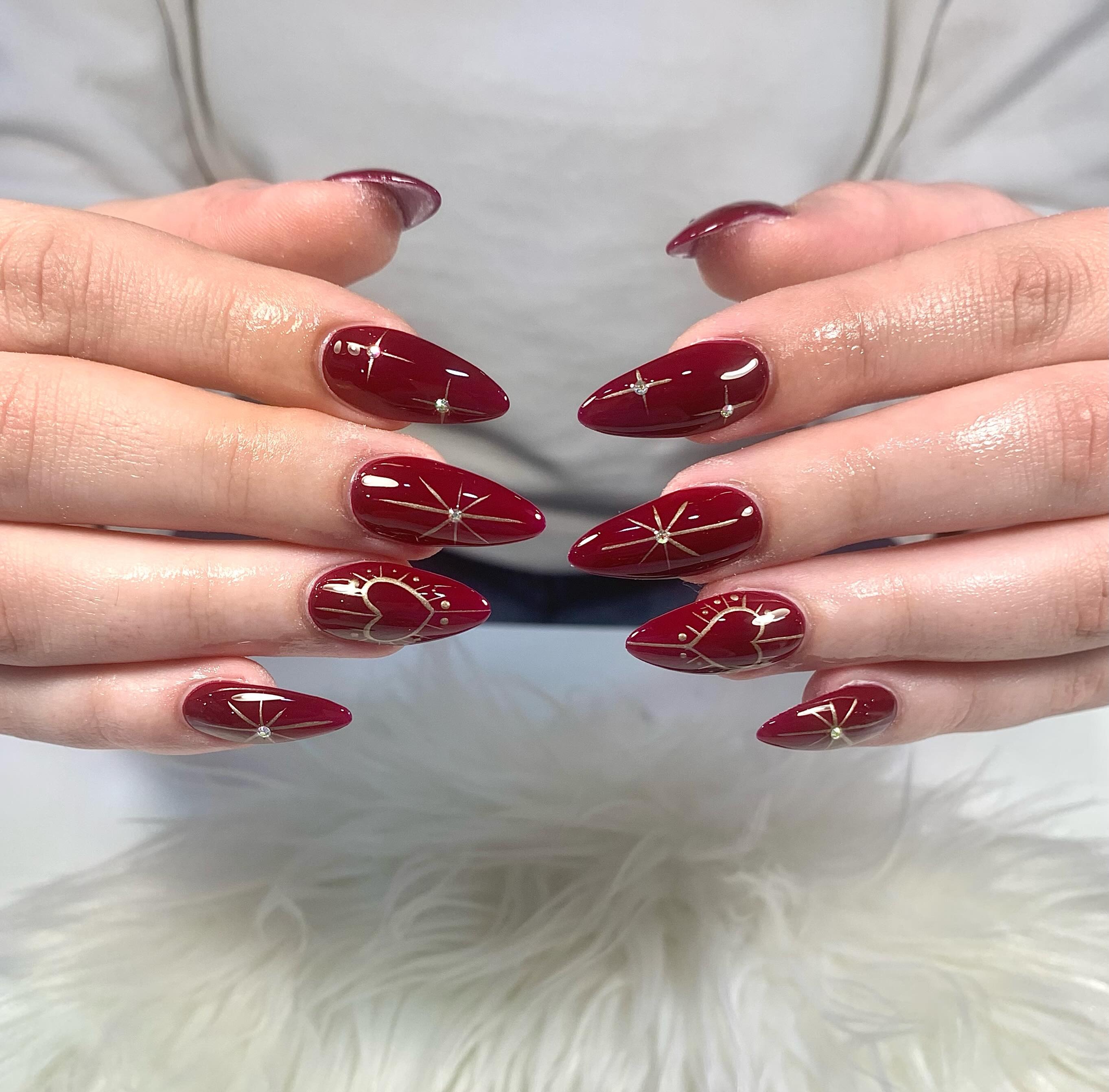 Manos con uñas acrílicas largas en forma almendrada, esmalte burdeos y estrellas y lunas doradas