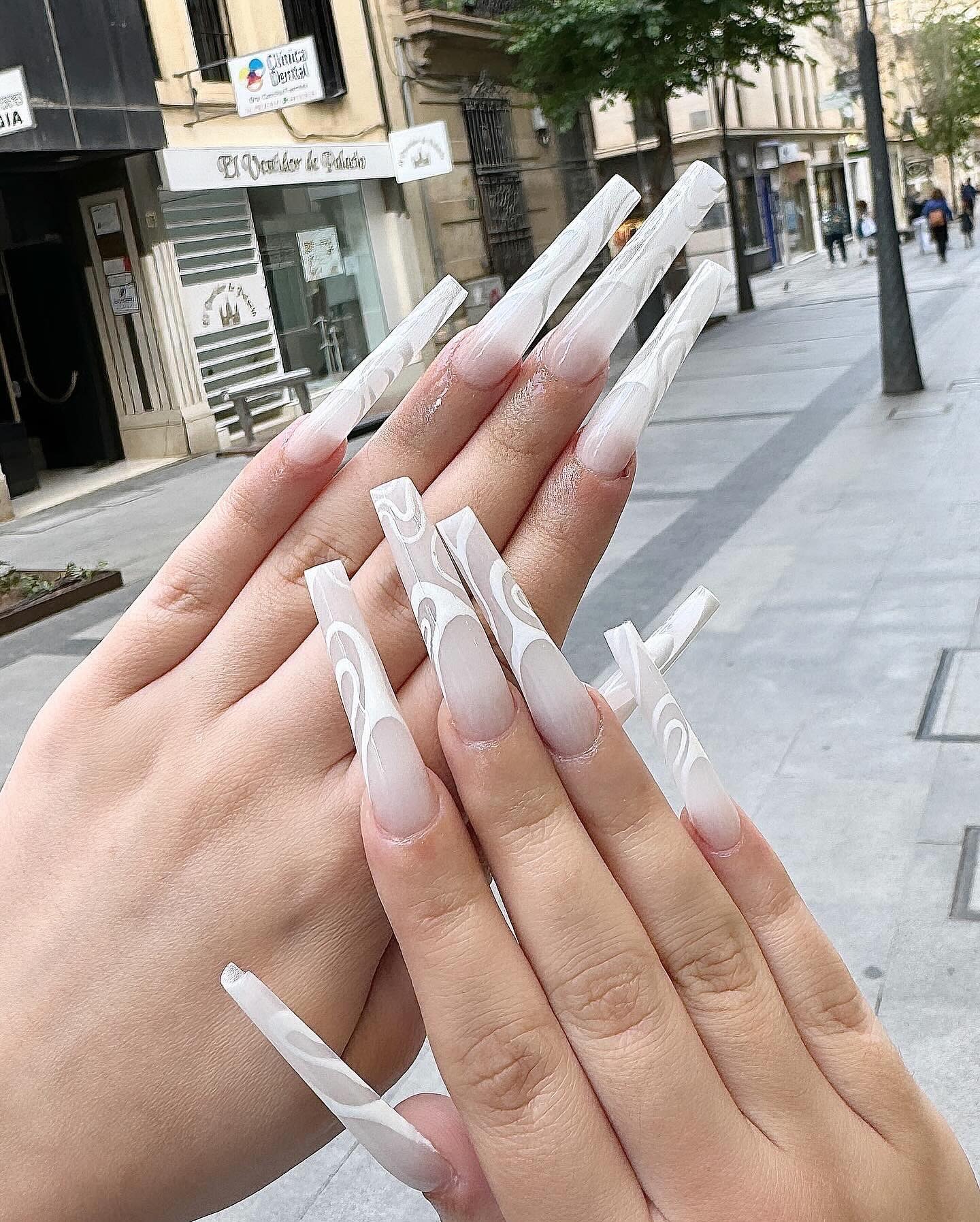 Uñas acrílicas coffin muy largas en degradado rosa a blanco con decoraciones doradas geométricas, en la calle