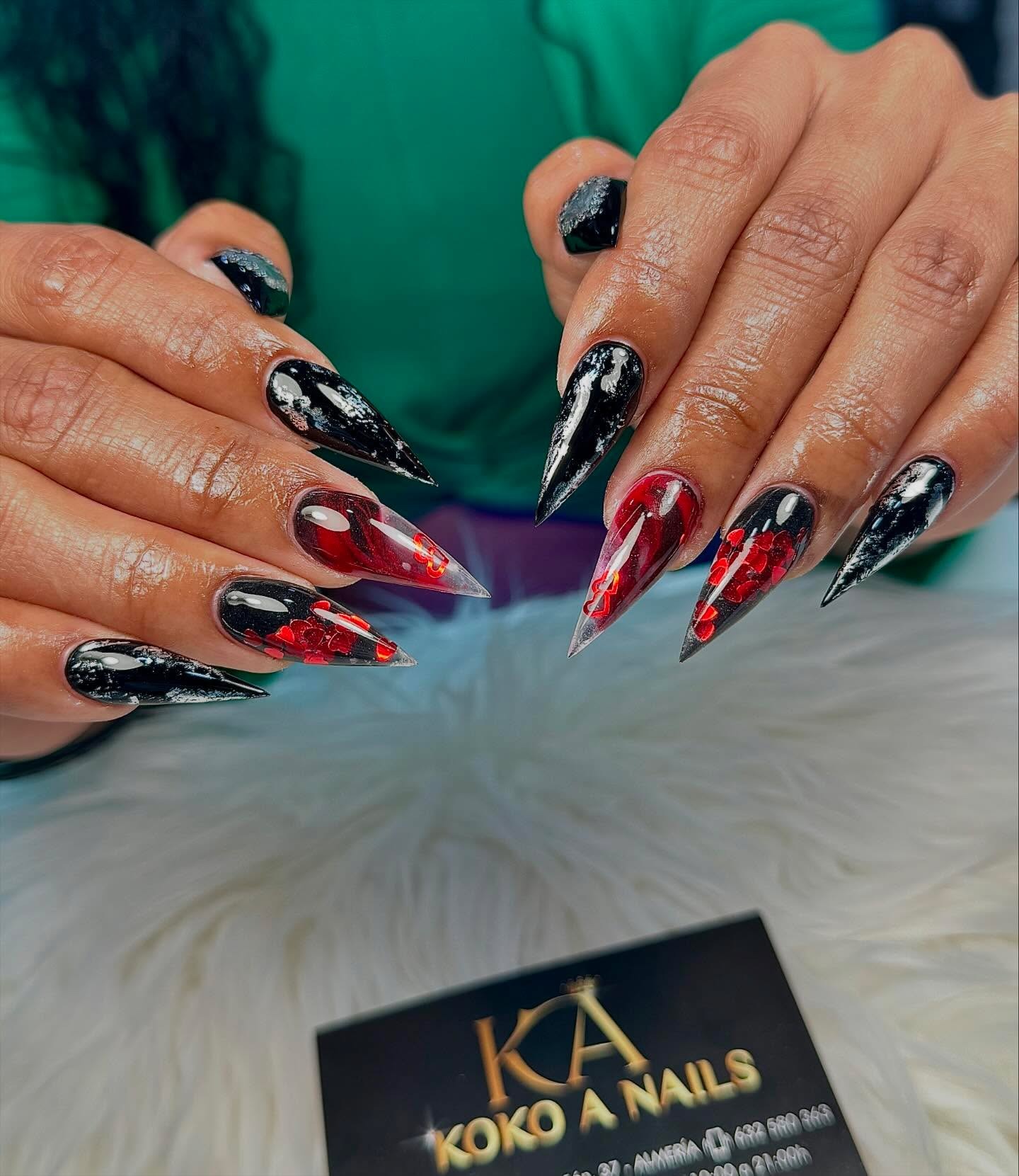 Uñas stiletto largas en negro y rojo con efecto mármol y purpurina, con la tarjeta de Koko A Nails