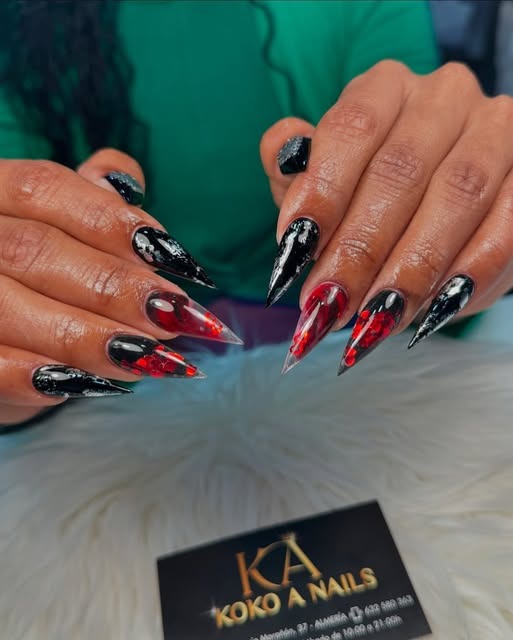 Uñas stiletto negras y rojas con efecto mármol y purpurina plateada, tarjeta de Koko A Nails al lado